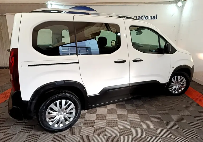 Vue de profil côté droit d'un Peugeot Rifter blanc 2019 avec barres de toit et protections noires sur les bas de caisse.