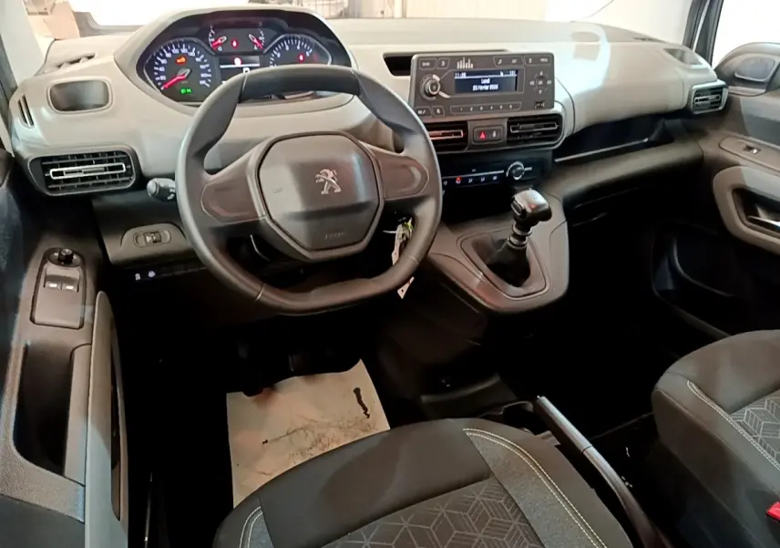 Vue intérieure avant du Peugeot Rifter blanc 2019, volant, tableau de bord numérique et levier de vitesse manuel visibles.