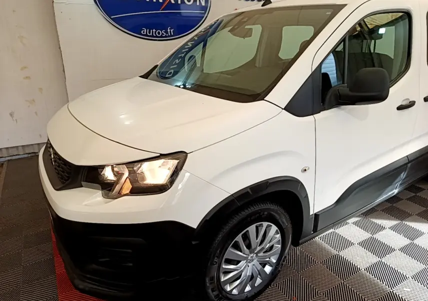 Vue 3/4 avant droit d'un Peugeot Rifter blanc avec phares allumés et protections noires sur les bas de caisse.