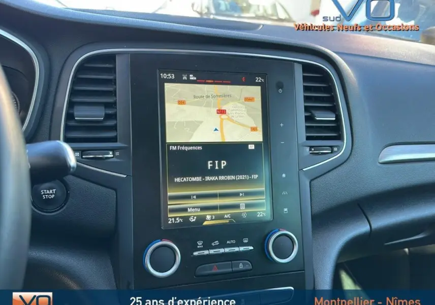 Vue rapprochée du tableau de bord de la Renault Mégane IV beige, avec écran tactile affichant la navigation et la radio FIP.