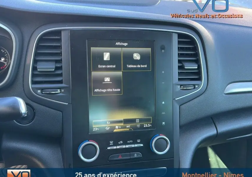Vue rapprochée de la console centrale noire de la Renault Mégane IV beige, affichant l'écran tactile et commandes climatisation.
