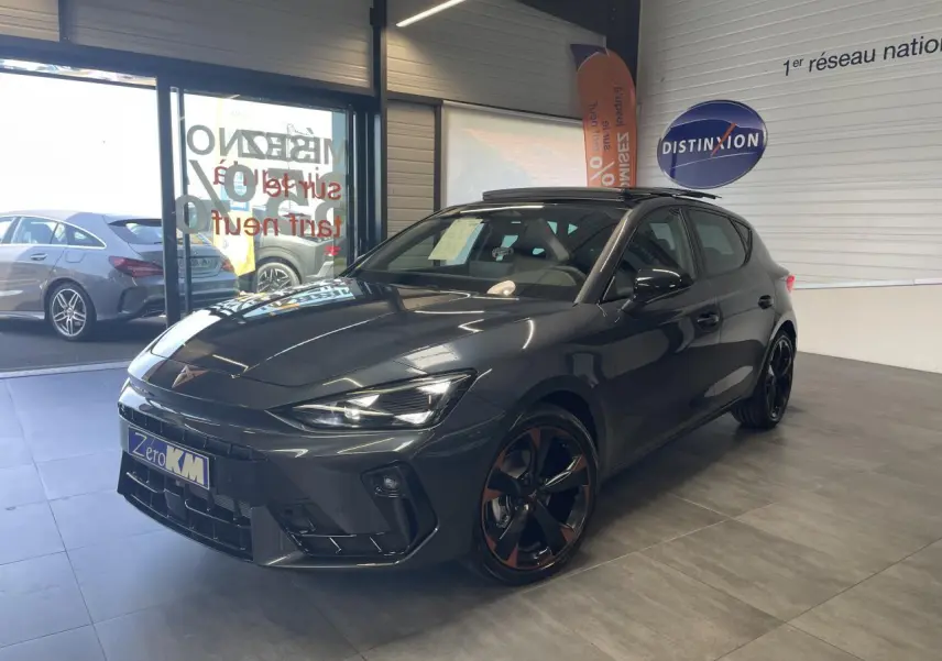 Vue 3/4 avant d'une CUPRA Leon gris magnetic avec jantes cuivrées et toit ouvrant panoramique en showroom.