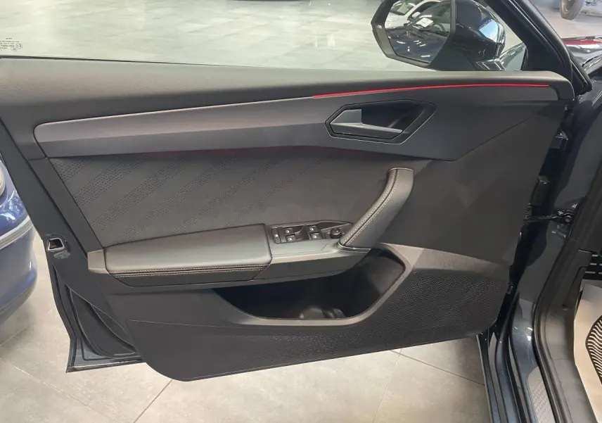 Vue côté gauche de la porte avant d'une CUPRA Leon 2026 gris magnetic avec contre-portes en suédine noire et surpiqûres cuivrées.
