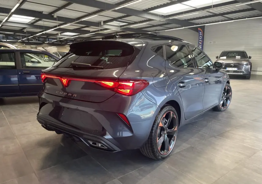 Vue 3/4 arrière droite d'une CUPRA Leon gris magnetic avec feux arrière Tri-LED et jantes cuivrées 18 pouces.