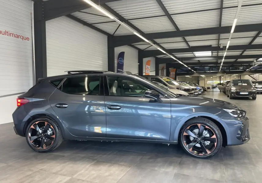 Vue de profil côté gauche d'une CUPRA Leon gris magnetic avec jantes alliage 18'' cuivrées en showroom.