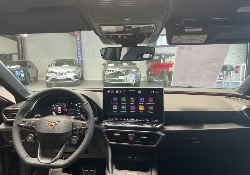 Vue intérieure avant du poste de conduite de la CUPRA Leon 2026 avec tableau de bord noir et écran tactile central.