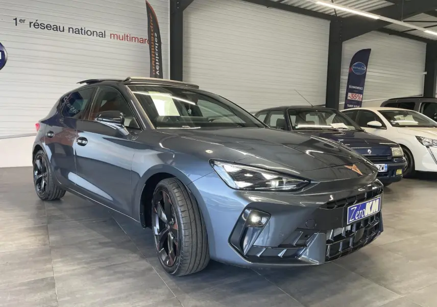 Vue 3/4 avant d'une CUPRA Leon 2.0 TDI gris magnetic avec jantes cuivrées dans un showroom intérieur.