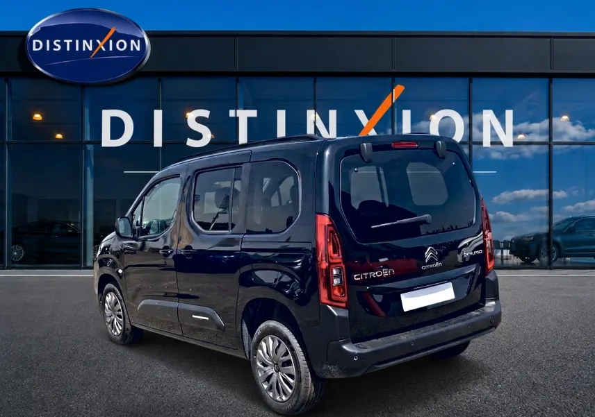 Vue 3/4 arrière droite d’un Citroën Berlingo noir 2026 avec vitres teintées et jantes alu devant un showroom.