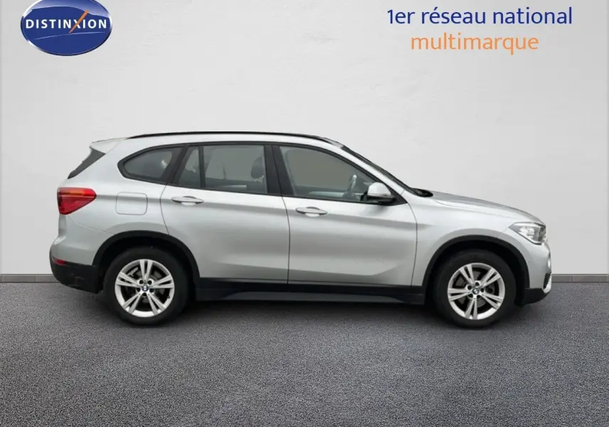 BMW X1 18i gris argent métal vu de profil côté gauche, avec jantes alliage 17 pouces et cinq portes visibles.