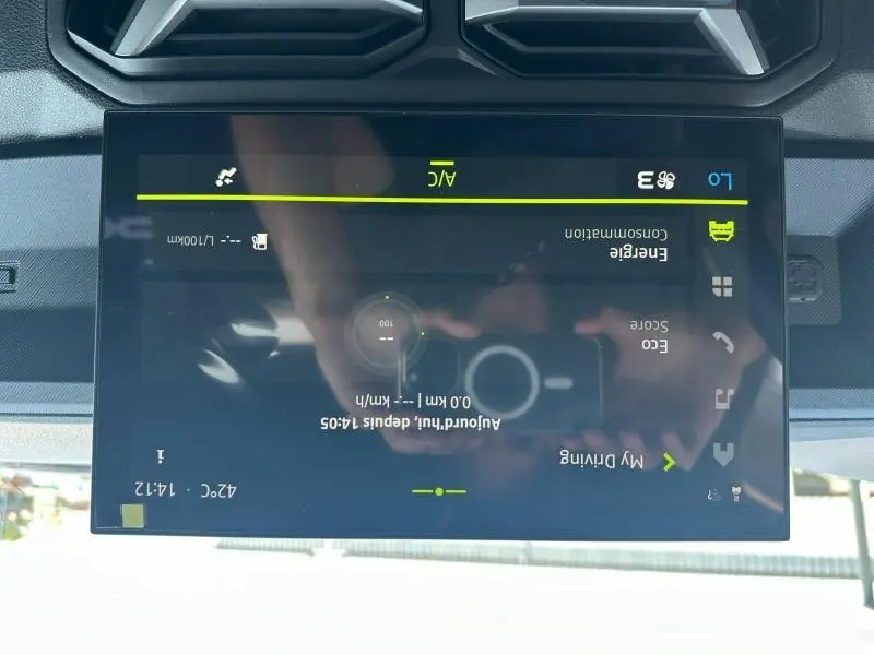 Écran tactile central du tableau de bord du Dacia Duster blanc, affichant les réglages de climatisation et consommation.