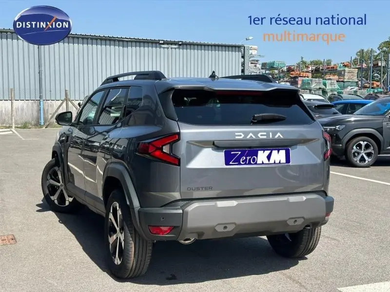 Vue 3/4 arrière d'un Dacia Duster gris métallisé avec jantes alliage et toit noir, stationné en extérieur.