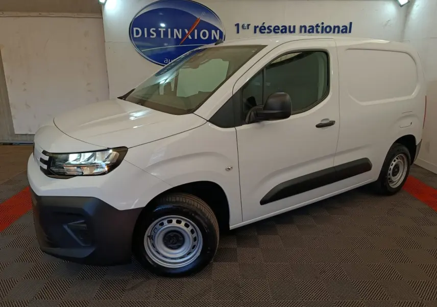 Vue 3/4 avant droit d’un Peugeot Partner blanc 2026 avec pare-chocs noir et jantes acier en intérieur showroom.