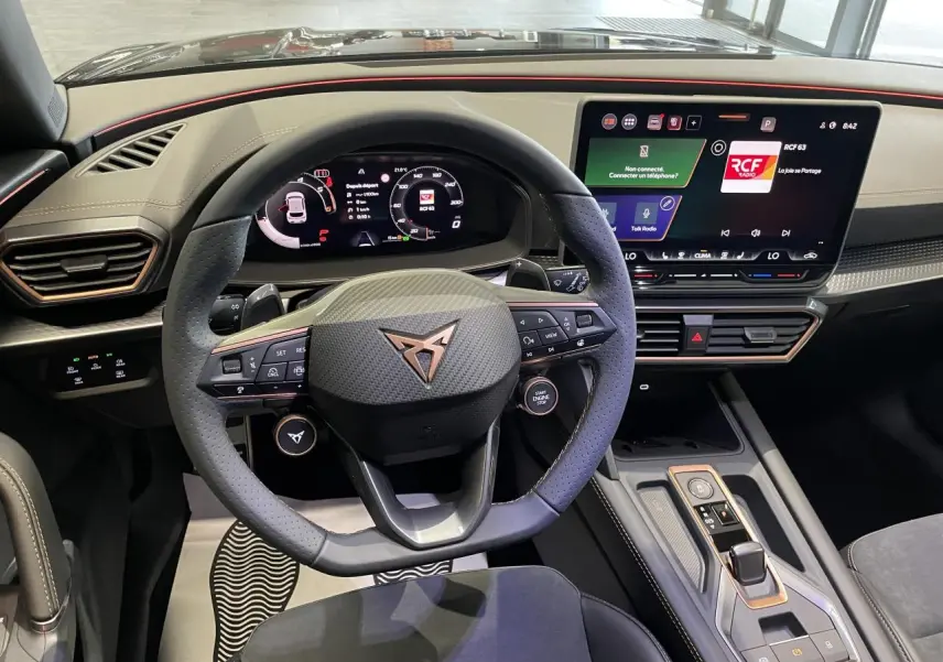 Intérieur CUPRA Leon 2026 vu du poste de conduite, volant cuir noir avec logo cuivré et écran tactile HD 12,9 pouces.