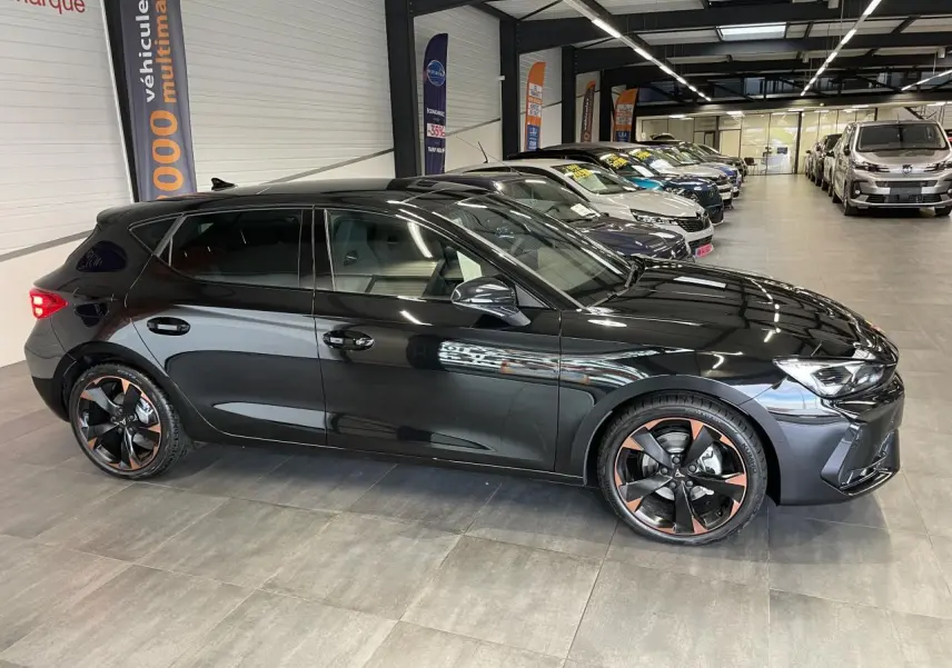 Vue de profil côté gauche d'une CUPRA Leon noire avec jantes alliage 18'' cuivrées dans un showroom.