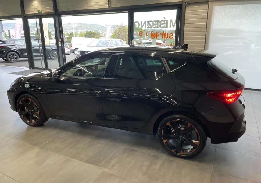 Vue de profil côté gauche d'une CUPRA Leon noire avec jantes alliage cuivrées dans un showroom lumineux.