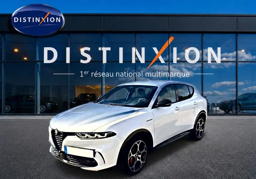 Vue 3/4 avant d'une Alfa Romeo Tonale blanche avec jantes alu distinctives, stationnée devant une vitrine Distinxion.