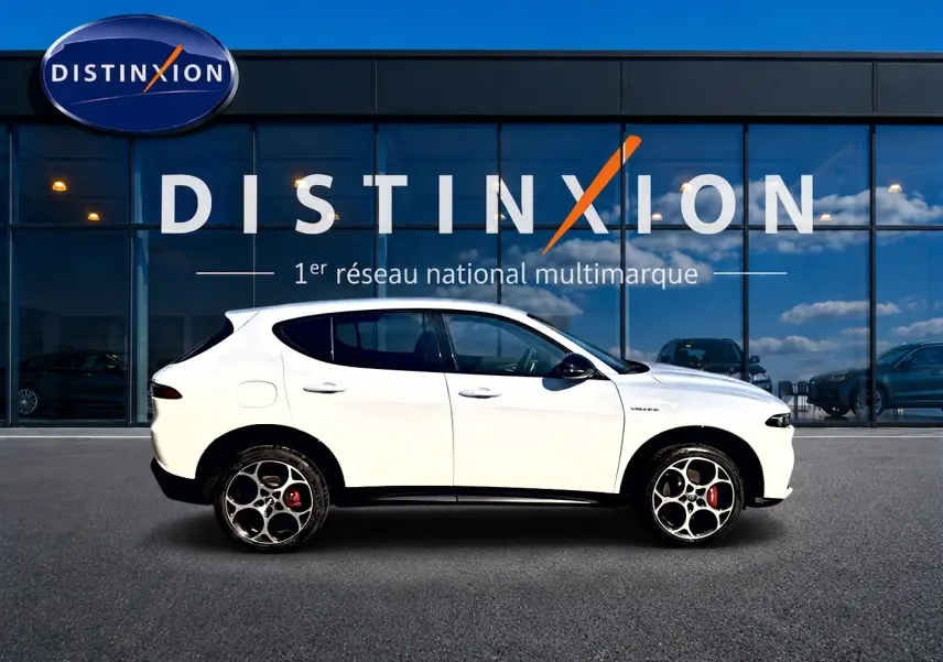 Vue de profil côté gauche d'un Alfa Romeo Tonale blanc avec jantes alu et étriers rouges, devant une vitrine Distinxion.
