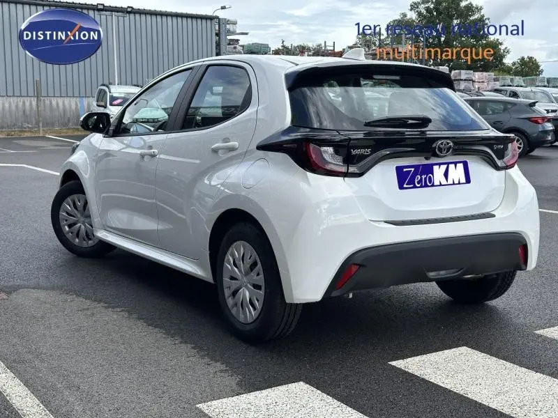 Toyota Yaris 116h Dynamic blanche vue 3/4 arrière droit, avec hayon noir et feux arrière distinctifs.