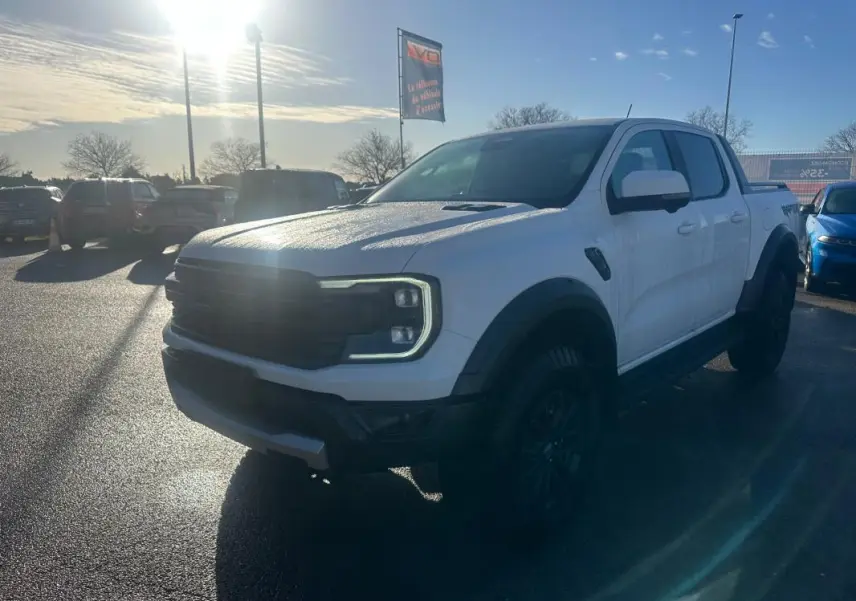 Ford Ranger Raptor blanc en 3/4 avant droit, avec calandre noire et jantes alliage noires visibles au soleil.