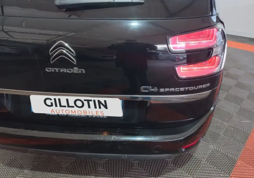 Vue arrière droite d'un Citroën Grand C4 Spacetourer noir avec feux arrière allumés et logo visible.