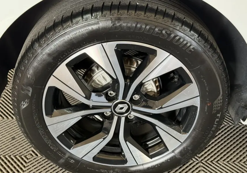 Gros plan sur la jante alliage bicolore noir et argent avec logo Renault au centre, pneu Bridgestone monté sur Clio blanche.