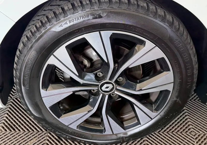 Gros plan sur la jante alliage bicolore et pneu d’une Renault Clio blanche, partie avant gauche visible.