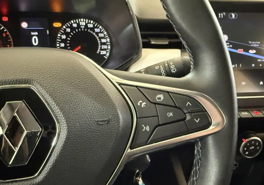 Gros plan sur le volant cuir synthétique noir de la Renault Clio Business, avec commandes multifonctions et tableau de bord partiel.