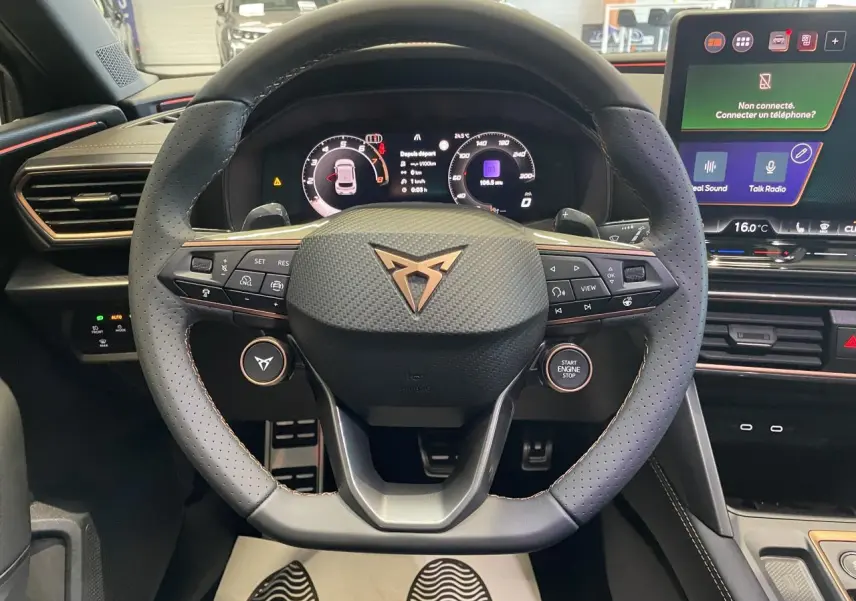 Vue centrée sur le volant perforé noir avec logo Cupra cuivré, tableau de bord digital et écran tactile HD à droite.