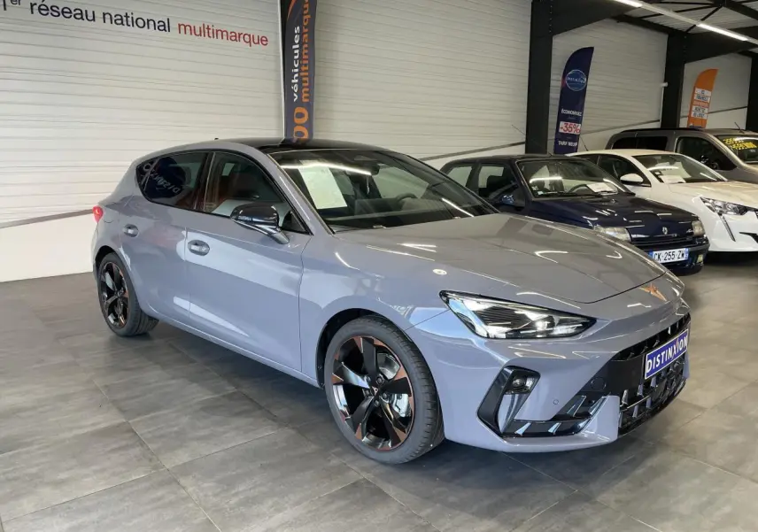 Vue 3/4 avant d'une CUPRA Leon gris Graphène avec jantes alliage noires et cuivrées en showroom.
