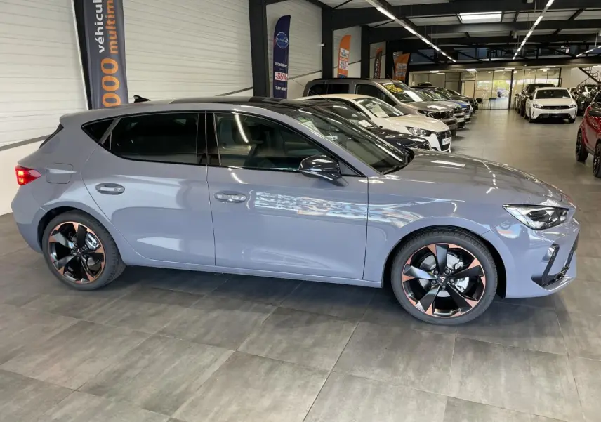 Vue latérale droite d'une CUPRA Leon 2026 gris Graphène avec jantes alliage noires et cuivrées en showroom.