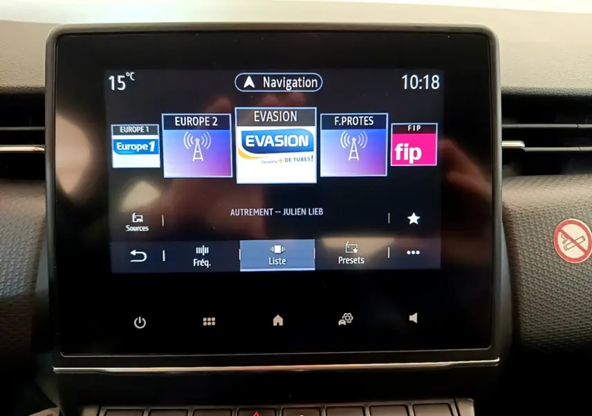 Écran tactile central de la Renault Clio Business blanche, affichant les radios et la navigation, vue de face.
