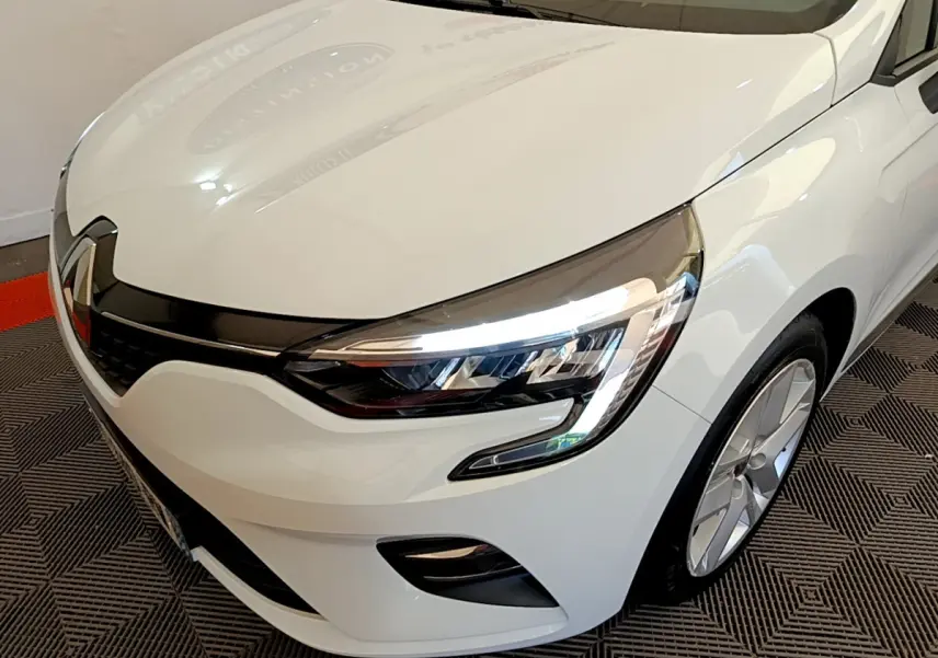 Vue 3/4 avant droit d'une Renault Clio Business blanche mettant en valeur ses phares LED et sa calandre noire brillante.