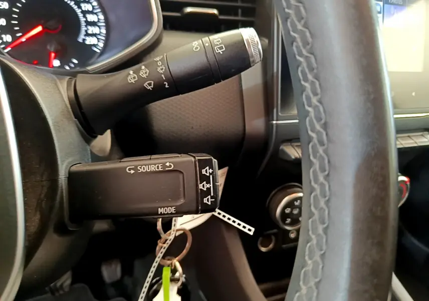 Gros plan sur le volant cuir et commandes au volant d'une Renault Clio Business blanche, tableau de bord partiellement visible.