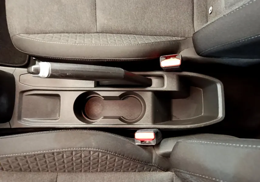 Vue plongeante sur la console centrale noire de la Renault Clio Business blanche avec frein à main et porte-gobelets.