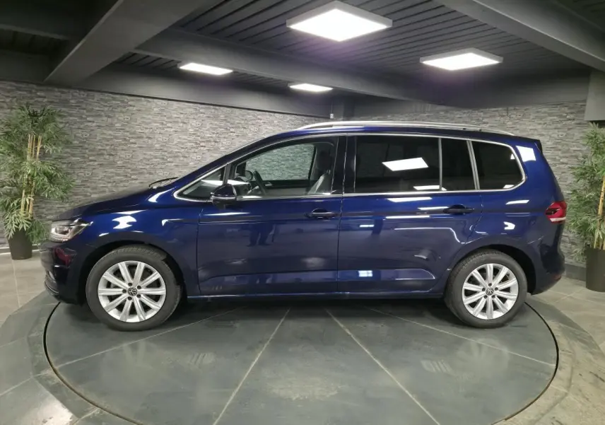 Profil côté gauche d'un Volkswagen Touran bleu métallisé 2024 dans un showroom avec jantes alliage 17 pouces.