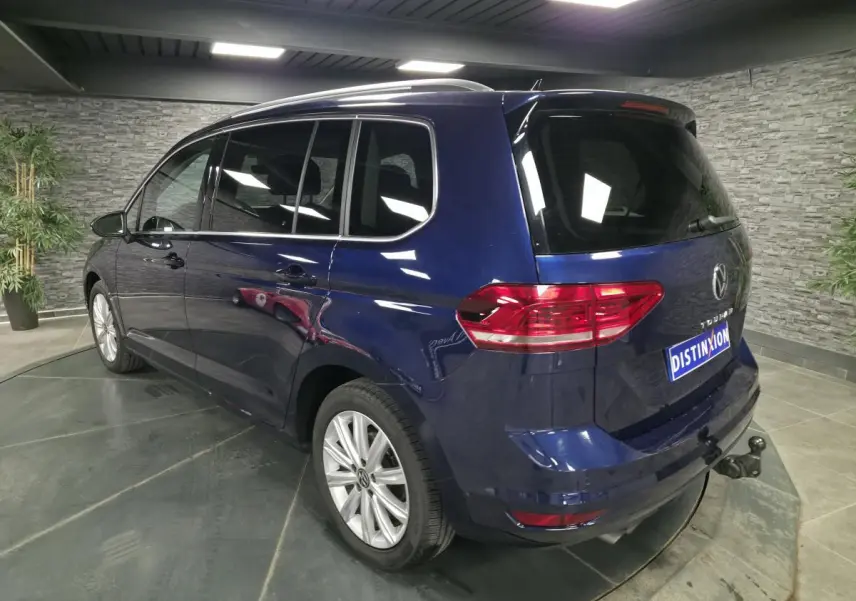 Vue 3/4 arrière droite d'un Volkswagen Touran bleu avec attelage escamotable en intérieur showroom.