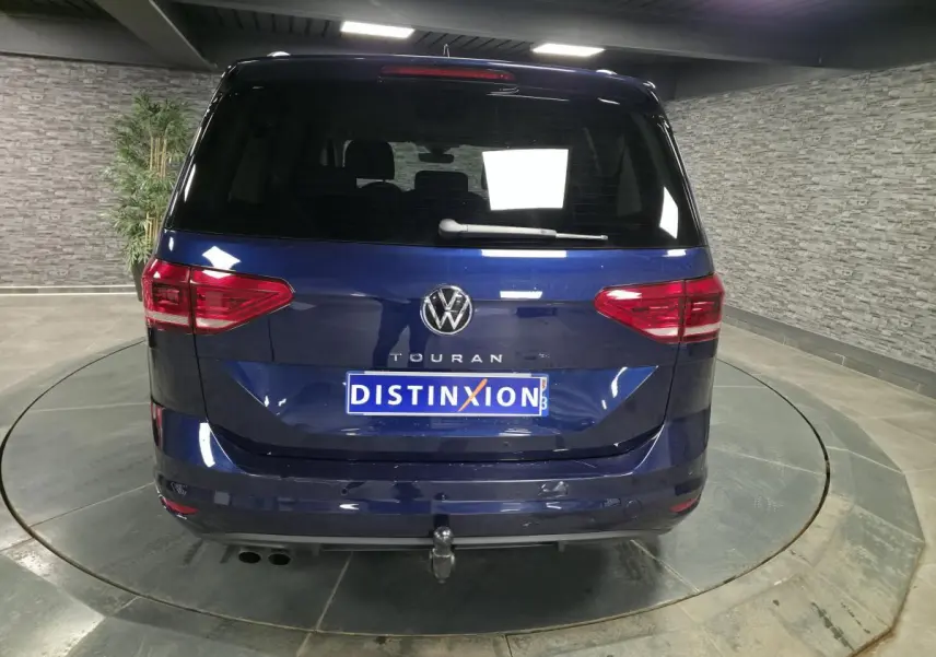 Vue arrière d'un Volkswagen Touran bleu 2024 avec crochet d'attelage escamotable et feux arrière LED.