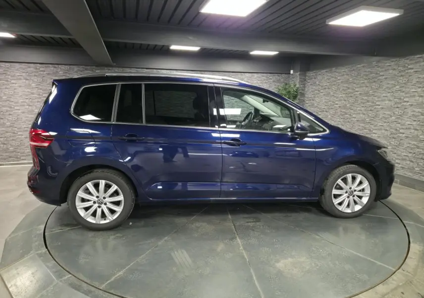 Profil côté gauche d'un Volkswagen Touran bleu métallisé 2024 dans un showroom avec jantes alliage 17 pouces.