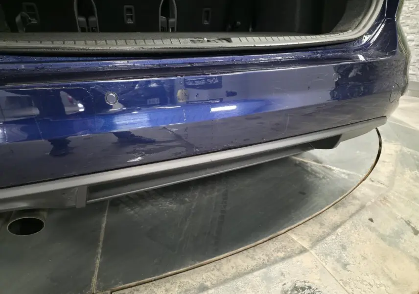 Gros plan sur le pare-chocs arrière bleu métallisé du Volkswagen Touran 2024 avec capteurs de recul visibles.