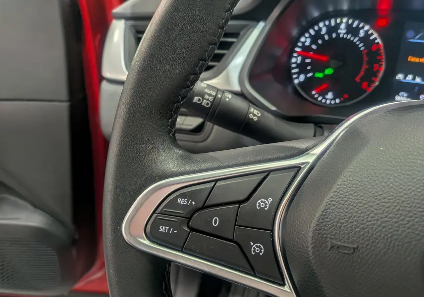 Gros plan sur le volant du Renault Captur Rouge Flamme 2023, montrant les commandes de régulateur de vitesse côté gauche.