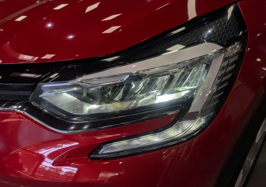 Gros plan sur le phare avant droit du Renault Captur TCe 90 CH Zen rouge flamme 2023, avec détails LED et carrosserie brillante.