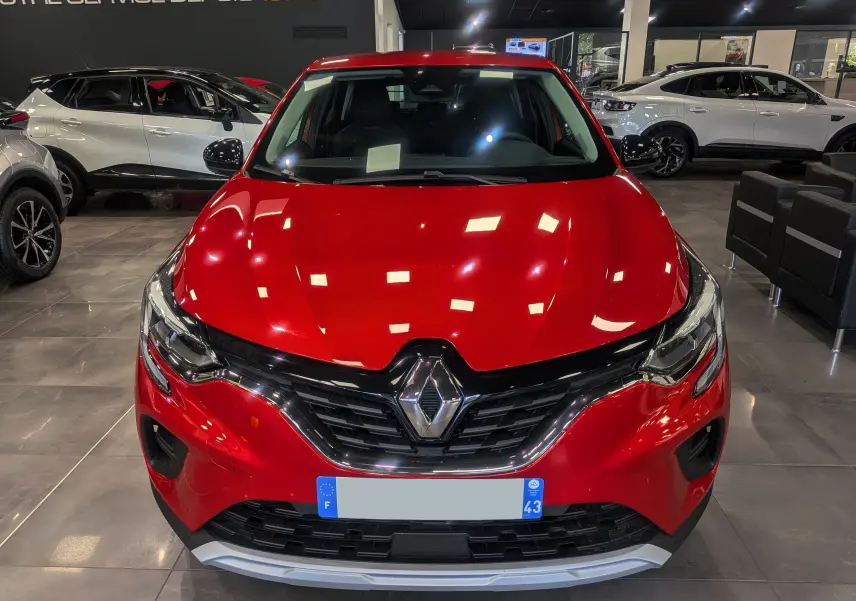 Vue frontale d'un Renault Captur TCe 90 CH ZEN rouge flamme, avec calandre noire et éclairage LED en showroom.