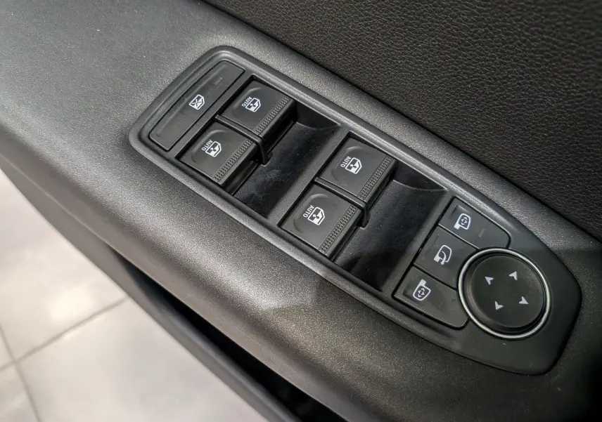 Gros plan sur les commandes de lève-vitres et réglages des rétroviseurs côté conducteur du Renault Captur rouge Flamme 2023.