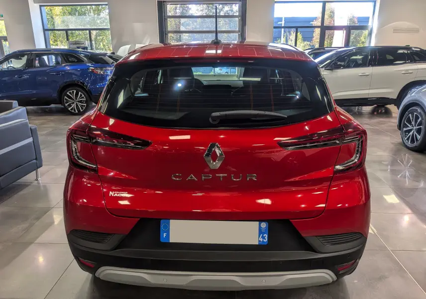 Vue arrière d'un Renault Captur Rouge Flamme 2023 dans un showroom, mettant en valeur ses feux effilés et son logo central.