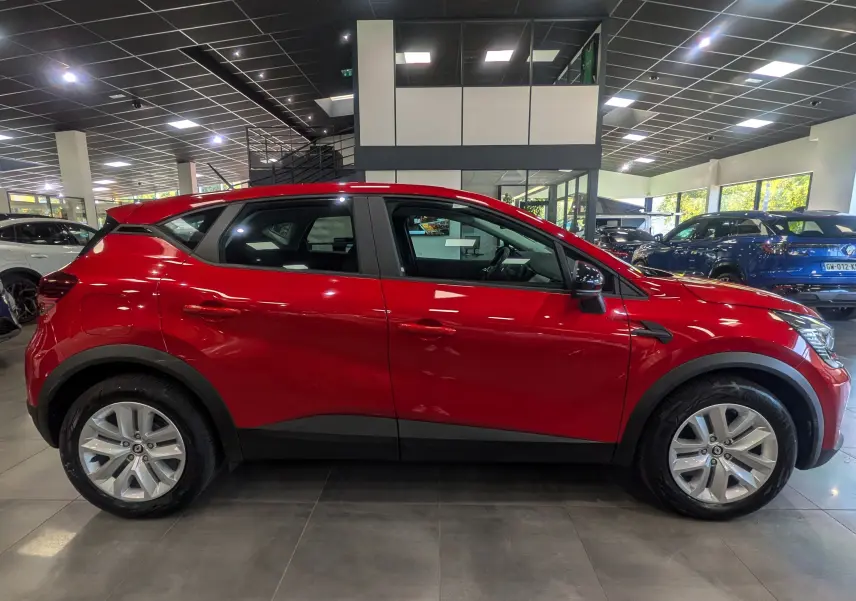 Profil côté gauche d'un Renault Captur Rouge Flamme 2023 en showroom, soulignant ses lignes modernes et ses jantes alliage.