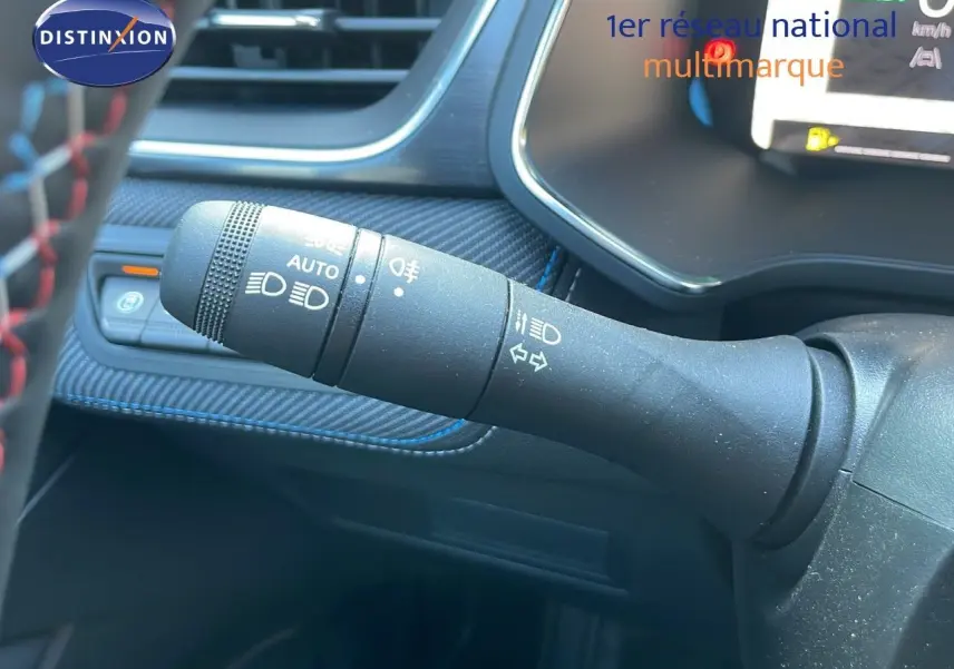 Gros plan sur la commande des feux et clignotants du Renault Captur E-Tech hybride 2025, intérieur noir avec surpiqûres bleues.