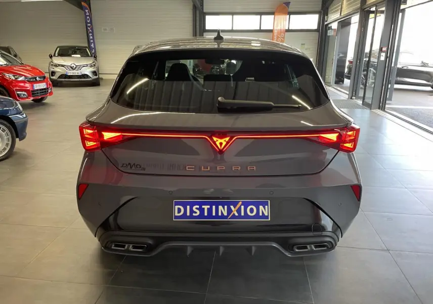 Vue arrière d'une CUPRA Leon gris Graphène avec feux arrière en bandeau lumineux et double sortie d'échappement noire.