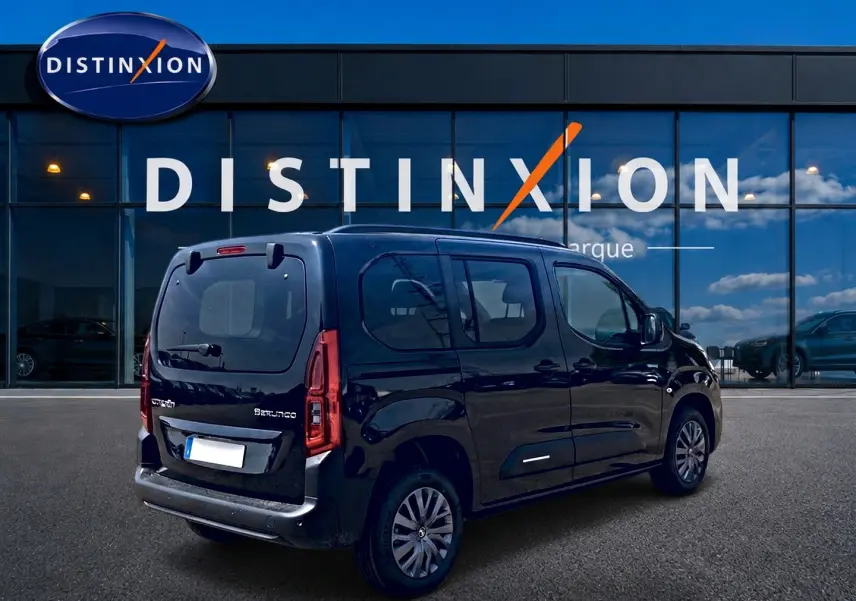 Vue 3/4 arrière droite d'un Citroën Berlingo noir avec barres de toit et jantes alu devant un bâtiment vitré.
