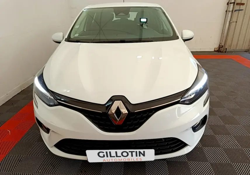 Vue frontale d'une Renault Clio Business blanche avec phares LED allumés sur sol à damier noir et rouge.