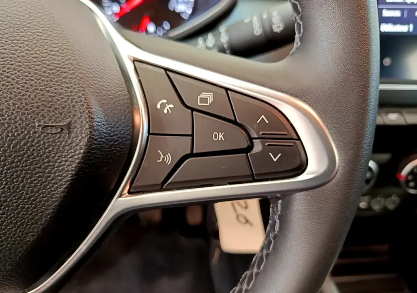 Gros plan sur les commandes du volant cuir noir de la Renault Clio Business blanche, avec tableau de bord et écran tactile en arrière-plan.